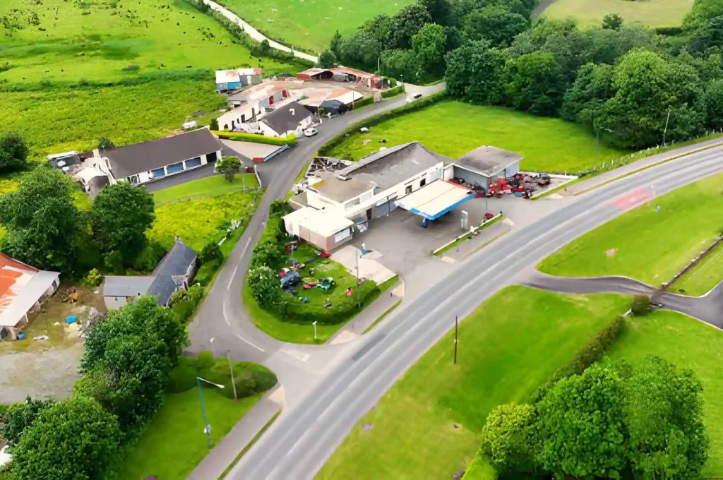 Aerial view of a gas station and small cluster of buildings surrounded by green fields in rural Linnyshaw.