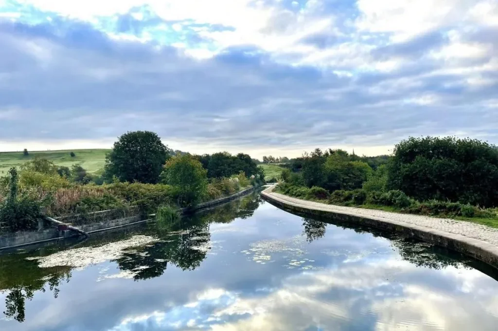 The still water of a scenic canal reflecting the cloudy sky in Little Lever.